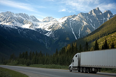 white freight truck running on concrete road near snow covered mountain at distance during daytime thumbnail