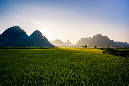 green grass field near mountain at sunrise thumbnail
