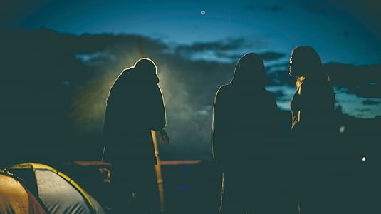 silhouette of three standing people beside tent during nighttime thumbnail