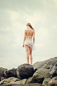 woman in white bikini standing on gray rocks at daytime thumbnail