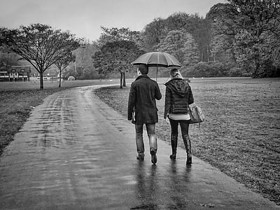 grayscale photo of couple walking on pavement while raining thumbnail