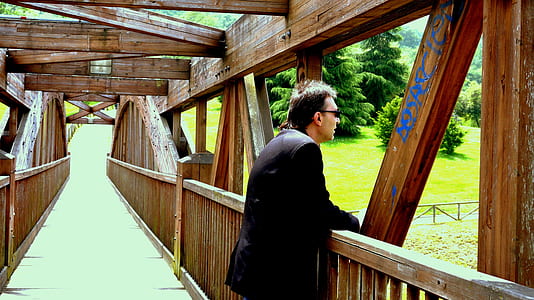 man standing on bride looking at green trees \ thumbnail