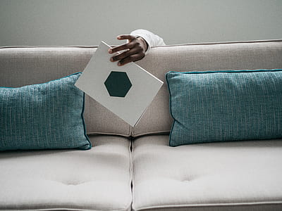 person hiding behind the sofa holding white with octagon shape print book thumbnail