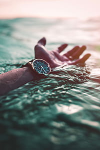 person's left hand wearing round black watch on body of water thumbnail
