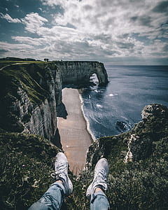 person sitting on cliff near body of water thumbnail