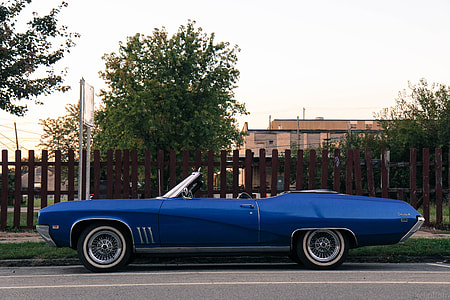 classic blue convertible coupe parked on roadside near brown wooden fence thumbnail