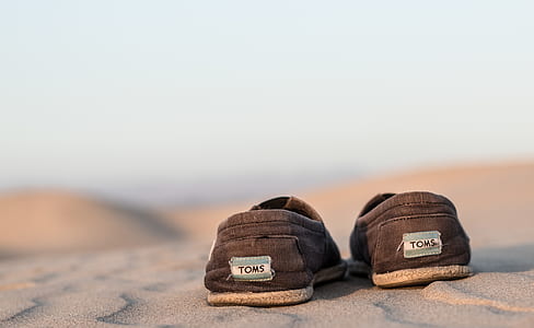 pair of black Toms shoes on sand thumbnail