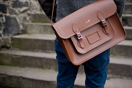 person wearing blue denim jeans and brown leather crossbody bag standing near grey concrete stair thumbnail