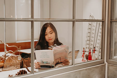 smiling woman reading book in front of window thumbnail