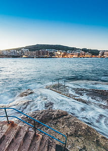 rippling ocean beside buildings under blue sky during daytime thumbnail