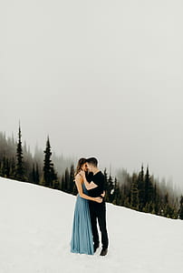 woman and man hugging in snow field behind the green trees under white cloudy sky ] thumbnail