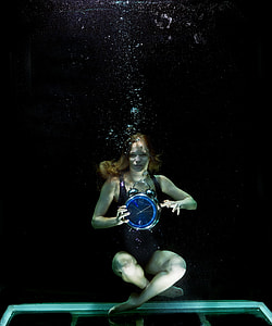 underwater photography of woman in black swim suit holding round blue desk clock thumbnail