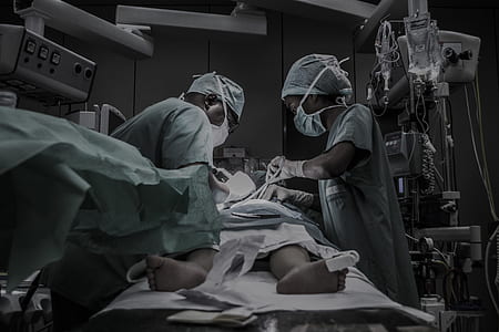 two surgeons operating on person lying on operating table inside operating room thumbnail
