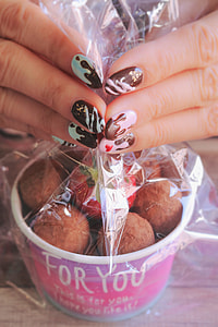 woman in blue, pink and black nail polish white holding chocolate ball plastic cover thumbnail