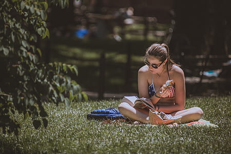 woman sitting on green grass while reading book thumbnail