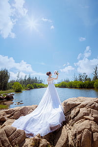 woman wearing wedding gown carrying bouquet of flowers on brown rock thumbnail