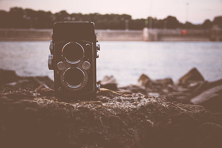 black and grey film camera on brown boulder near body of water thumbnail