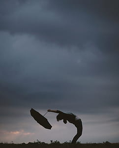 person bending his/her body while holding an umbrella thumbnail