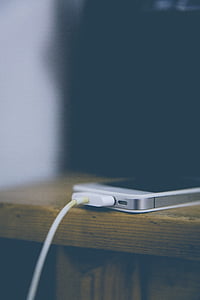 charging white iPhone 4 on brown wooden table thumbnail