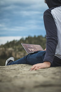 man sitting on mountain cliff under blue sky during daytime thumbnail