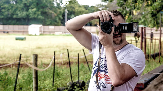 Man Holding Dslr Camera While Standing Near Fence thumbnail