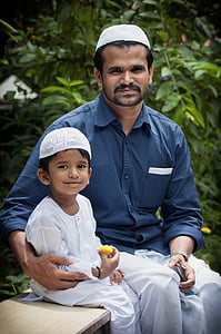 man in blue dress shirt sitting beside toddler in white thobe thumbnail