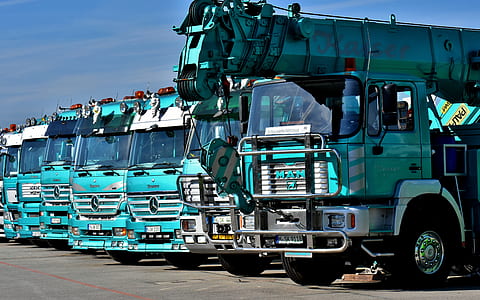 teal crane truck near dump trucks during daytime thumbnail