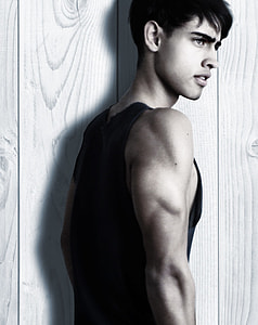 man in black tank top posing for photo beside wall thumbnail