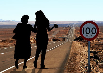 silhouette photo of two women walking down the street with 100 years signage thumbnail
