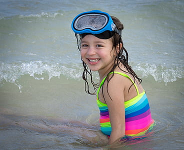 girl wearing multicolored striped top and blue swimming goggles on body of watr thumbnail