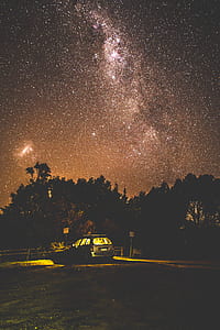 starry sky over black parked car surrounded with trees thumbnail
