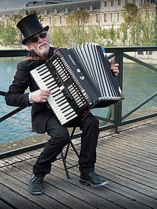 man playing accordion near body of water during daytime thumbnail