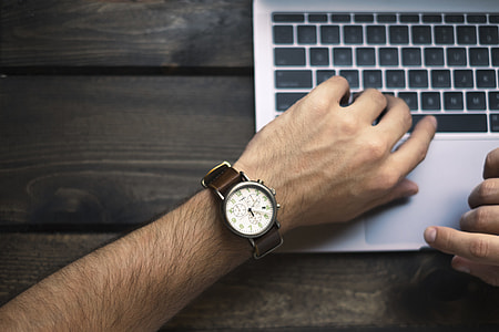 man in white analog watch holding silver laptop computer thumbnail