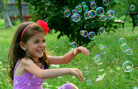 girl wearing pink dress sitting on grass near bubbles thumbnail