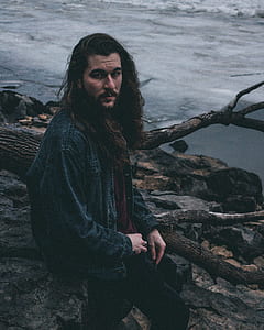 man sitting on tree branch near seashore during daytime thumbnail
