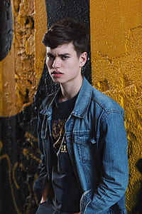 man wearing blue denim jacket beside yellow and black wall thumbnail