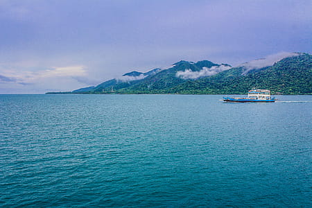 Blue and White Yacht on Teal Sea Near Green Mountain thumbnail