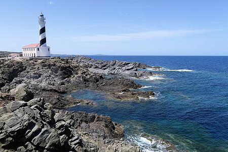 white and black lighthouse near cliff and body of water at daytime thumbnail