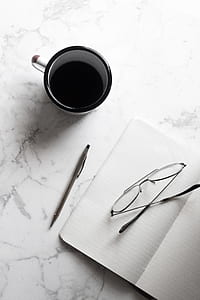 white and black ceramic mug beside notebook with pen and eyeglasses thumbnail