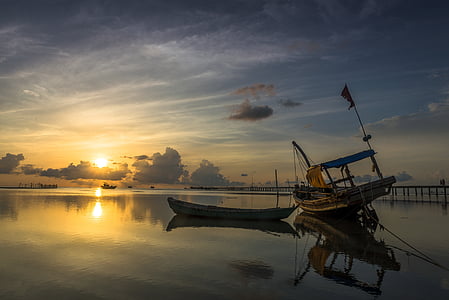 yellow center console boat beside brown canoe on body of water during sunset thumbnail