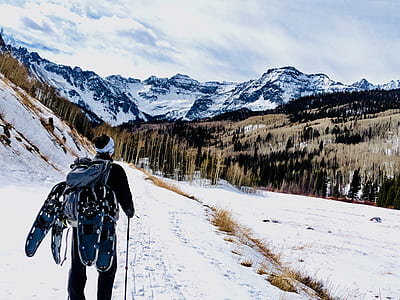 man standing on snow field facing mountain range thumbnail