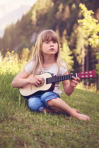 girl in white t-shirt playing beige and brown guitar on grass field during daytime thumbnail