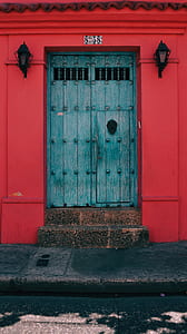 closed teal wood palette door between red walls and sconces thumbnail