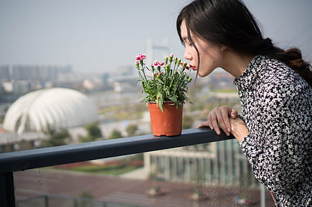 woman wearing white and black floral long-sleeved shirt kissing flower while standing during daytime thumbnail