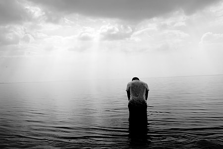 person wearing t-shirt sitting on body of water bowing down grayscale photography thumbnail