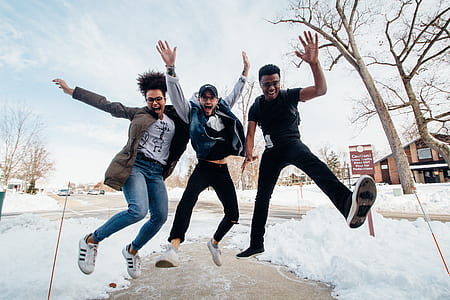 three people jumps on pathway in between snow covered ground during daytime thumbnail