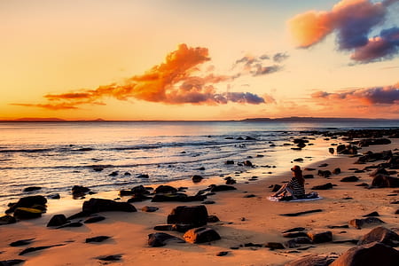 woman sitting on sand near body of water during dawm thumbnail