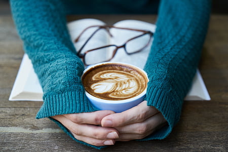 person's hand holding white ceramic coffee mug filled with latte thumbnail