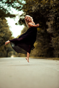 woman wearing black sleeveless dress in bare foot jumping in concrete road thumbnail