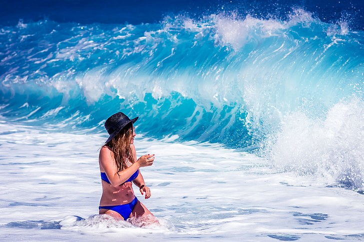 woman kneeling on seashore facing seawaves during daytime